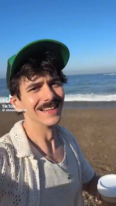 white man walking along beach speaking to the camera