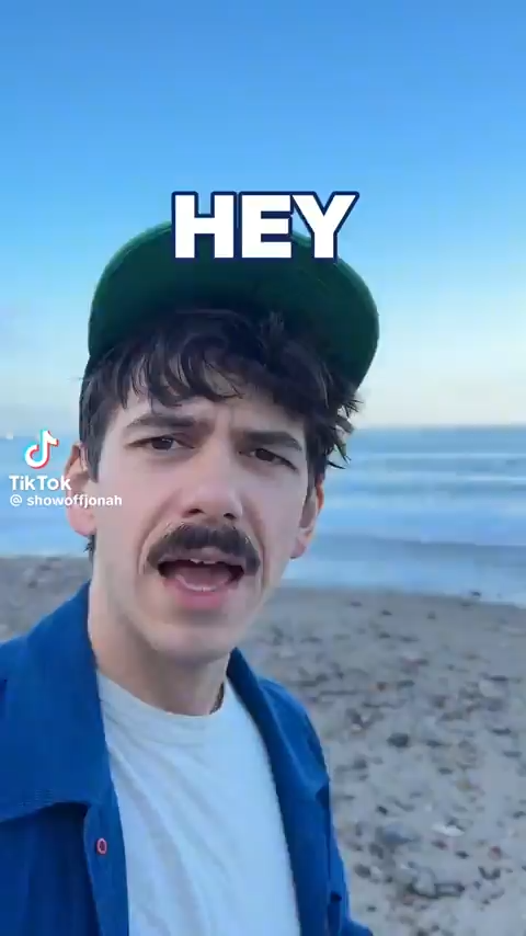 white man walking along beach and speaking into camera